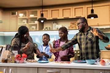 african american parents kids doing karaoke dancing together while cooking making homemade copy